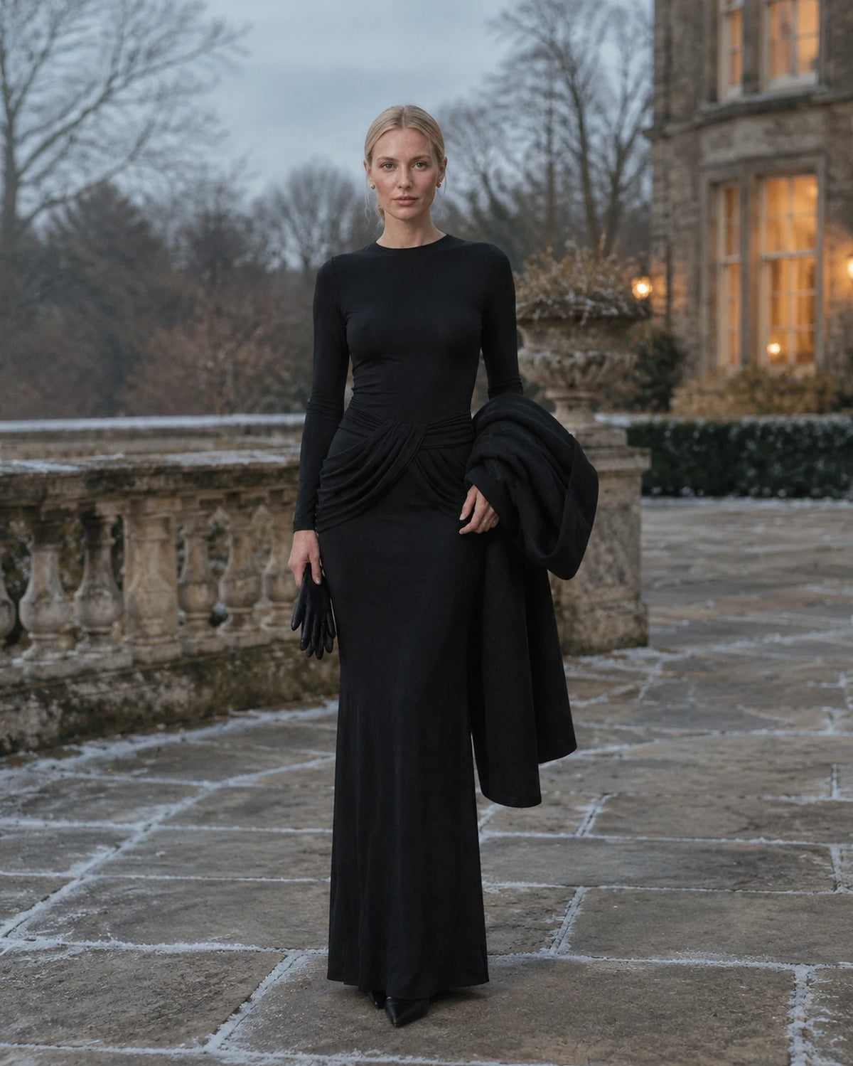 Woman in a black long-sleeve floor-length gown on a frosted stone terrace on a winter afternoon
