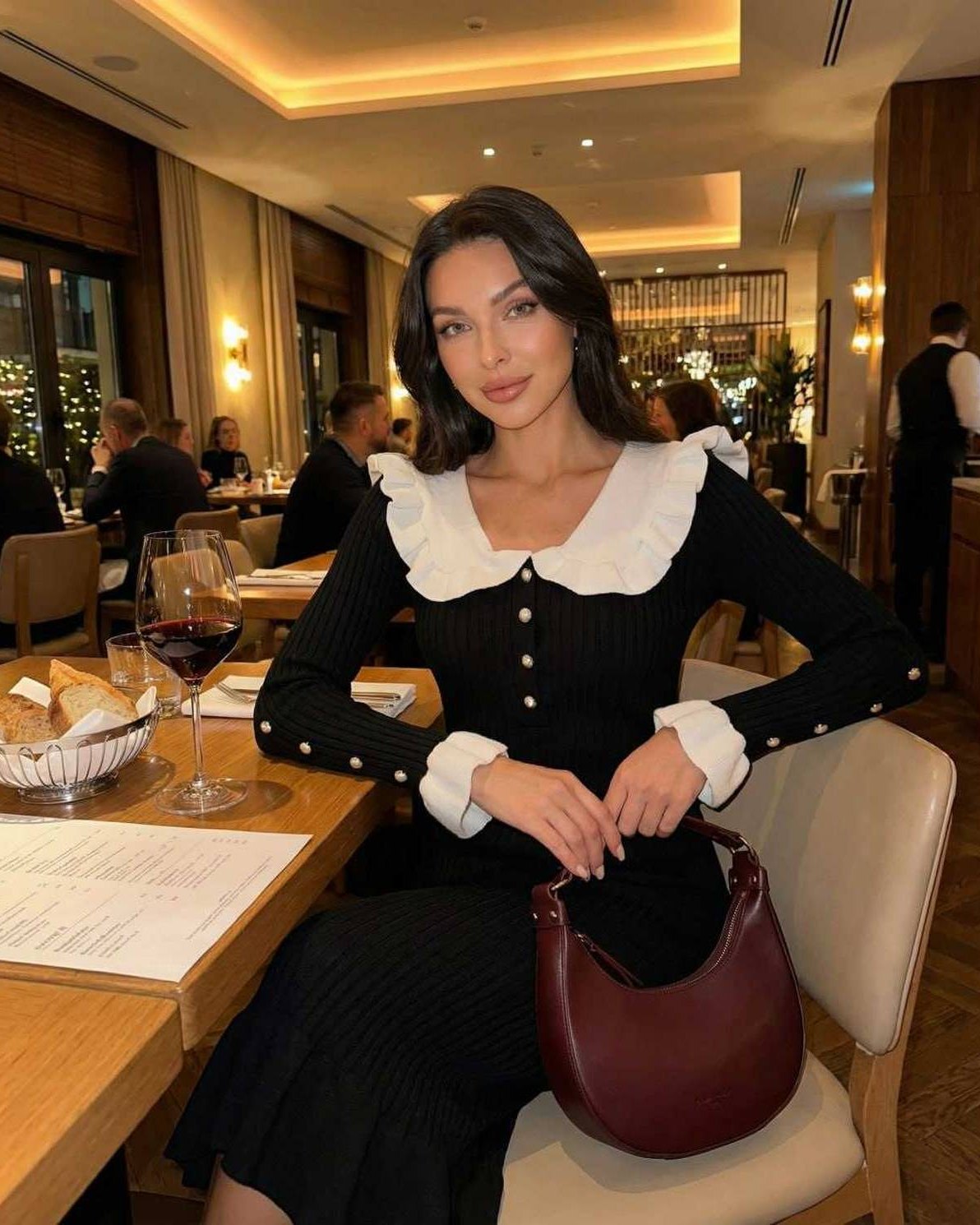 Model wearing Valencia Midi Dress by Lauven with ruffled collar in a restaurant setting.