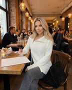 Aspen Sweater from Lauven, women’s white turtleneck sweater in a cozy restaurant setting.