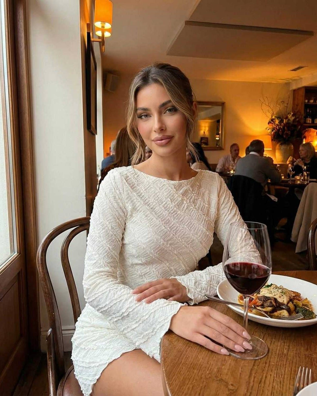 Sienna Mini Dress by Lauven worn by model in a restaurant, showcasing its textured white fabric and A-line silhouette.