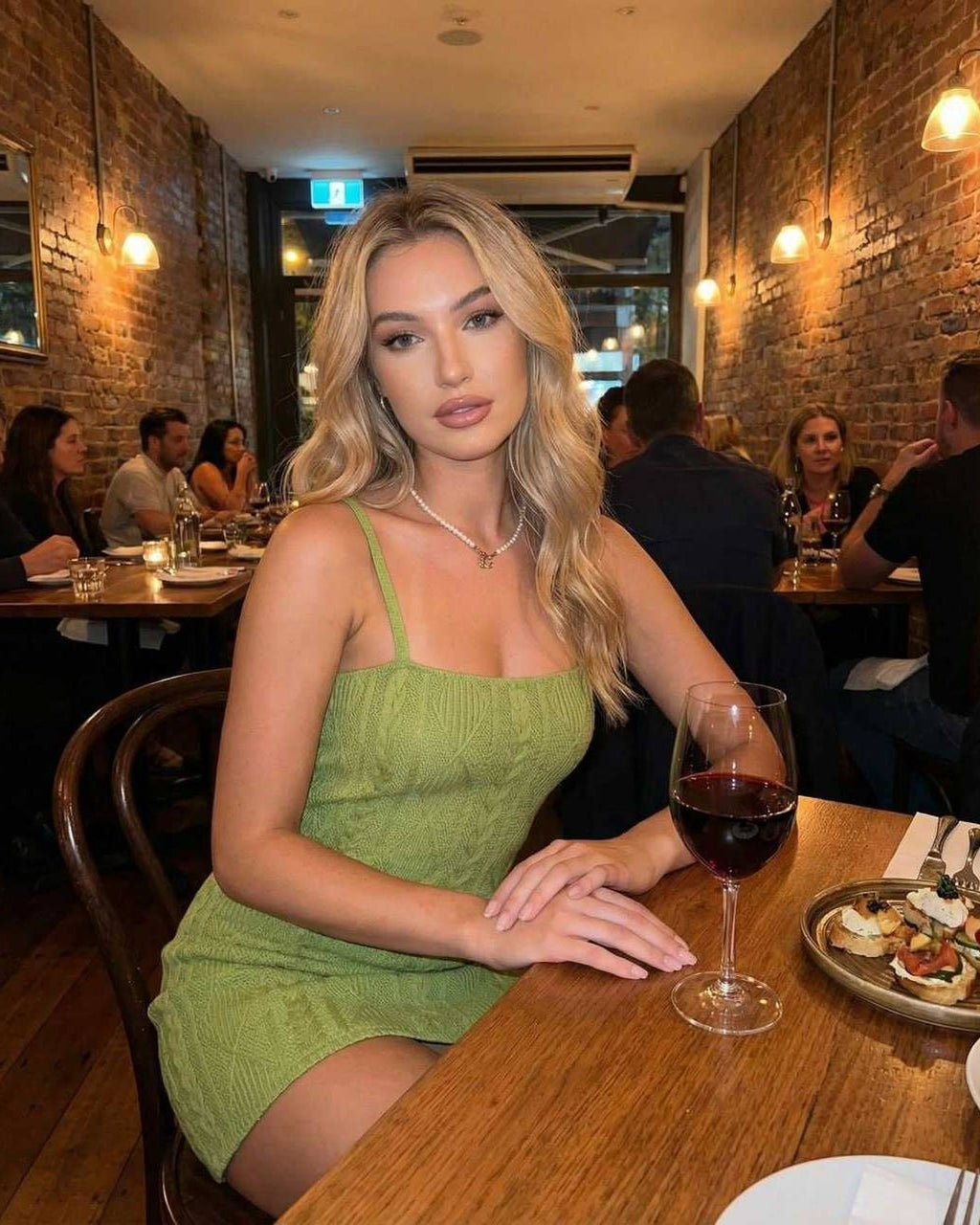 Lauven Verona Mini Dress in green on model sitting at a restaurant table with a drink, showcasing a stylish bodycon design.