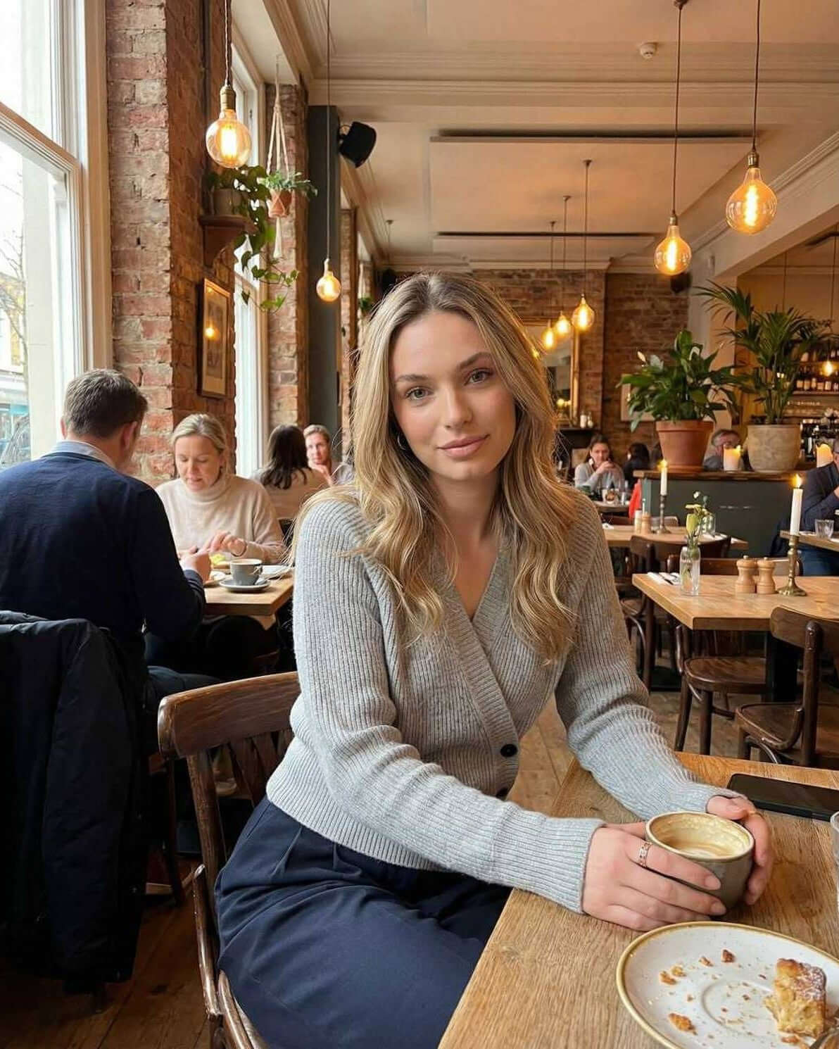 Woman wearing a gray Vienna Sweater by Lauven, sipping coffee in a cozy cafe setting.