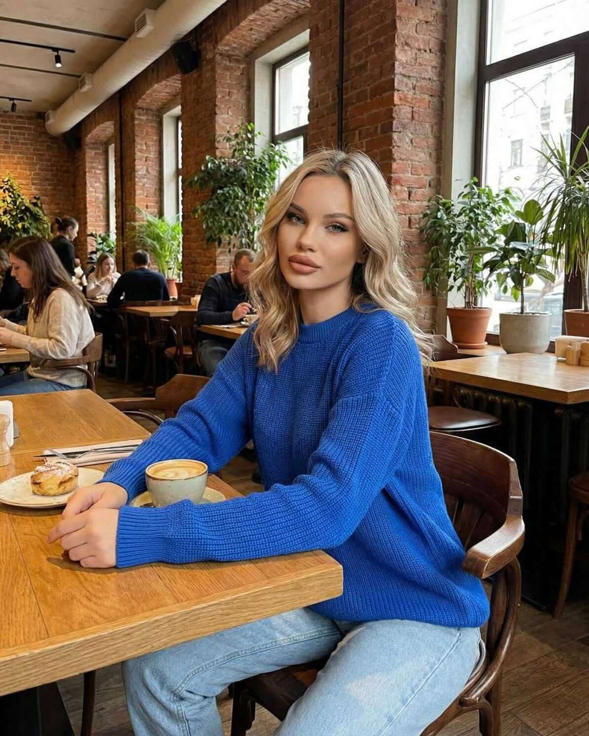 Monaco Sweater worn by a woman in a cafe, showcasing its vibrant blue color and relaxed fit by Lauven.