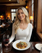 Elara Pullover – Woman enjoying a meal, wearing a white pullover sweater with lace trim in a cozy restaurant setting.
