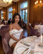 Elegant woman in Aurora Mini Dress by Lauven, off-shoulder satin design, dining in a luxurious restaurant setting.