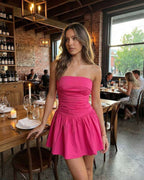 Azalea Mini Dress by Lauven in vibrant pink, showcasing a strapless A-line silhouette in a chic dining setting.