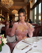 Elegant woman wearing a Blush Maxi Dress by Lauven, showcasing feather cuffs in a luxurious restaurant setting.