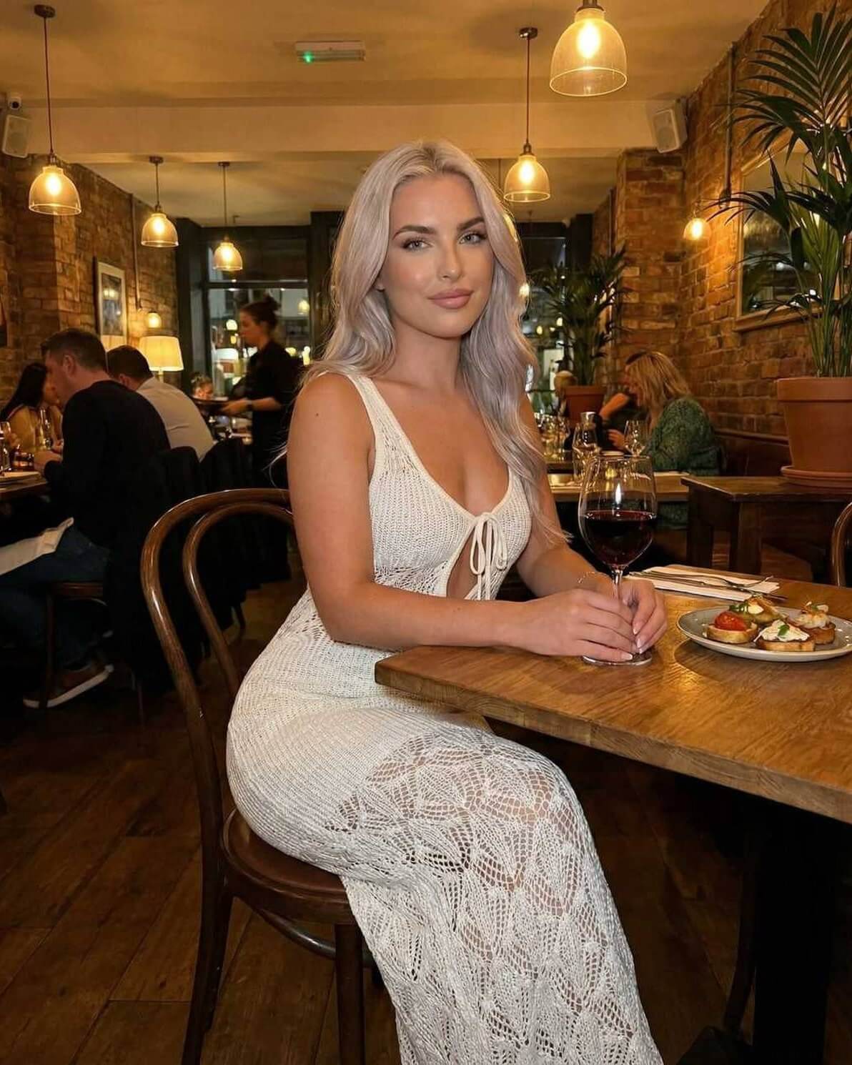 Celeste Maxi Dress by Lauven worn by a woman sitting at a restaurant, showcasing intricate crochet and tie-back design.