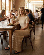 Woman enjoying a drink in a Celeste Maxi Dress by Lauven, seated in a stylish restaurant with a relaxed ambiance.