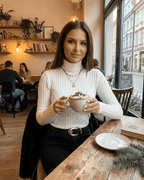 Elara Sweater by Lauven, a stylish ribbed turtleneck worn with a cozy drink in a cafe setting.