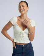 Elara Tie Top by Lauven, a ruched V-neck crop blouse with adjustable front tie detail, captured on a smiling model.
