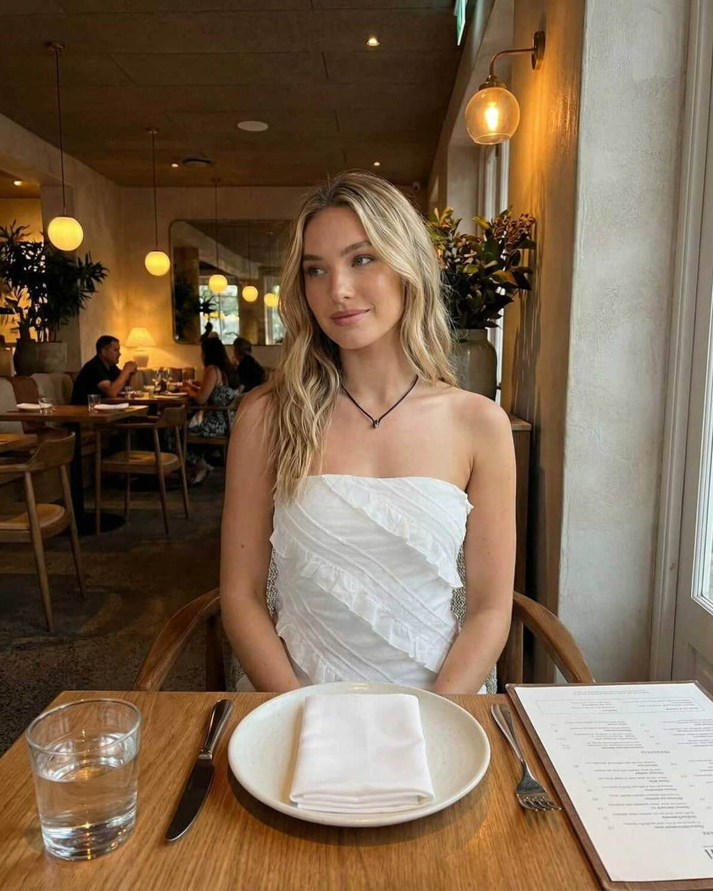 Isla Mini Dress by Lauven, an elegant strapless sheath dress with delicate ruffle details, showcased in a stylish dining setting.