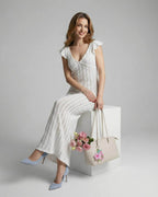 Model wearing Lauven Ivory Lace Maxi dress with ruffle sleeves, holding a bag and flowers.
