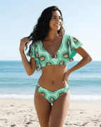 Lauven Kiwi Two-Piece Swimsuit in green kiwi print featuring flutter sleeves and a deep V-neckline on the beach.