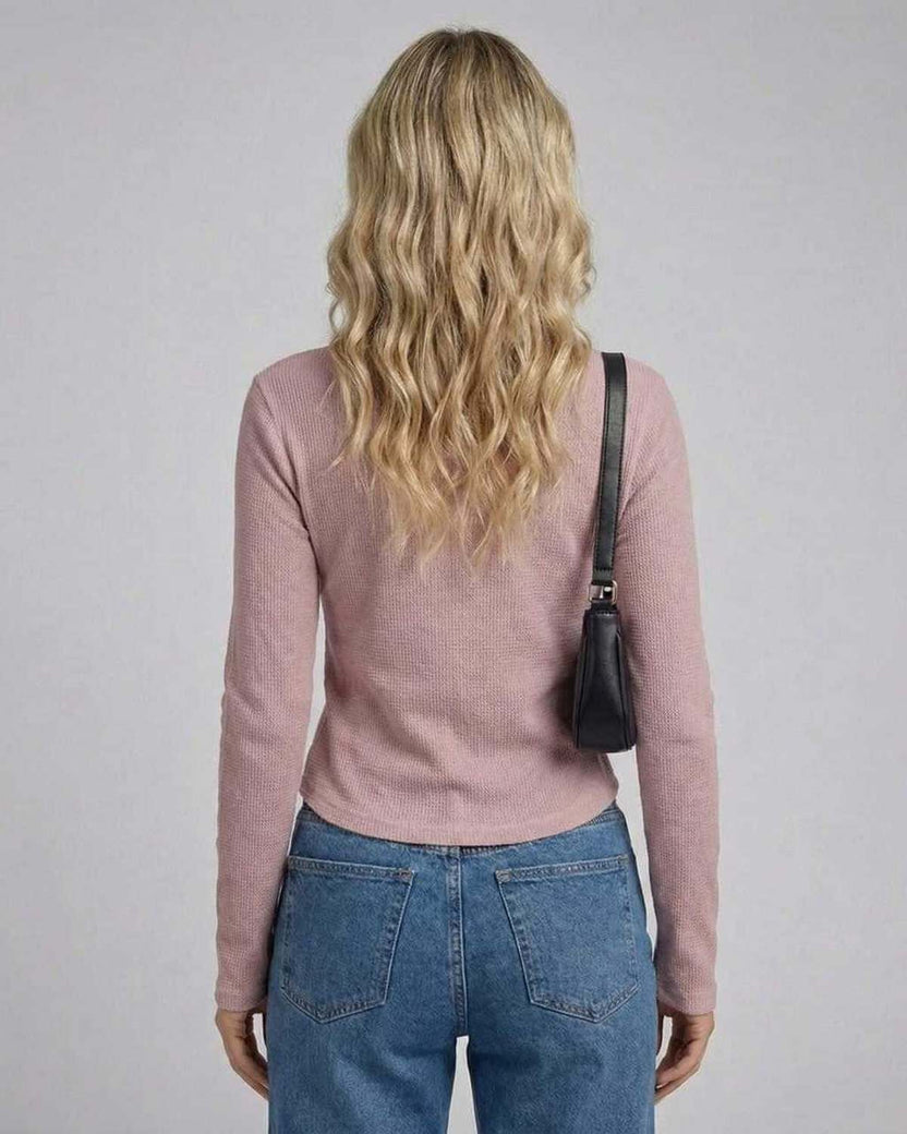 Back view of a woman wearing the Arden Long Sleeve top in dusty rose, paired with jeans and a small black bag.