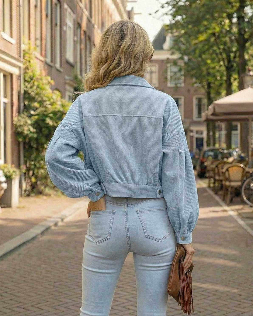 Back view of a woman wearing the Lauven Aurora Jacket, a blue cropped jacket with lantern sleeves, in a stylish outdoor setting.