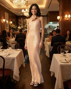 Elegant woman wearing a Lauven Blush Maxi Dress in a restaurant, showcasing the halter neckline and sequin sheath silhouette.