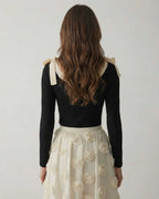 Back view of a model wearing the Lauven Camellia Pullover, a black knit sweater with bow detail, paired with a floral skirt.