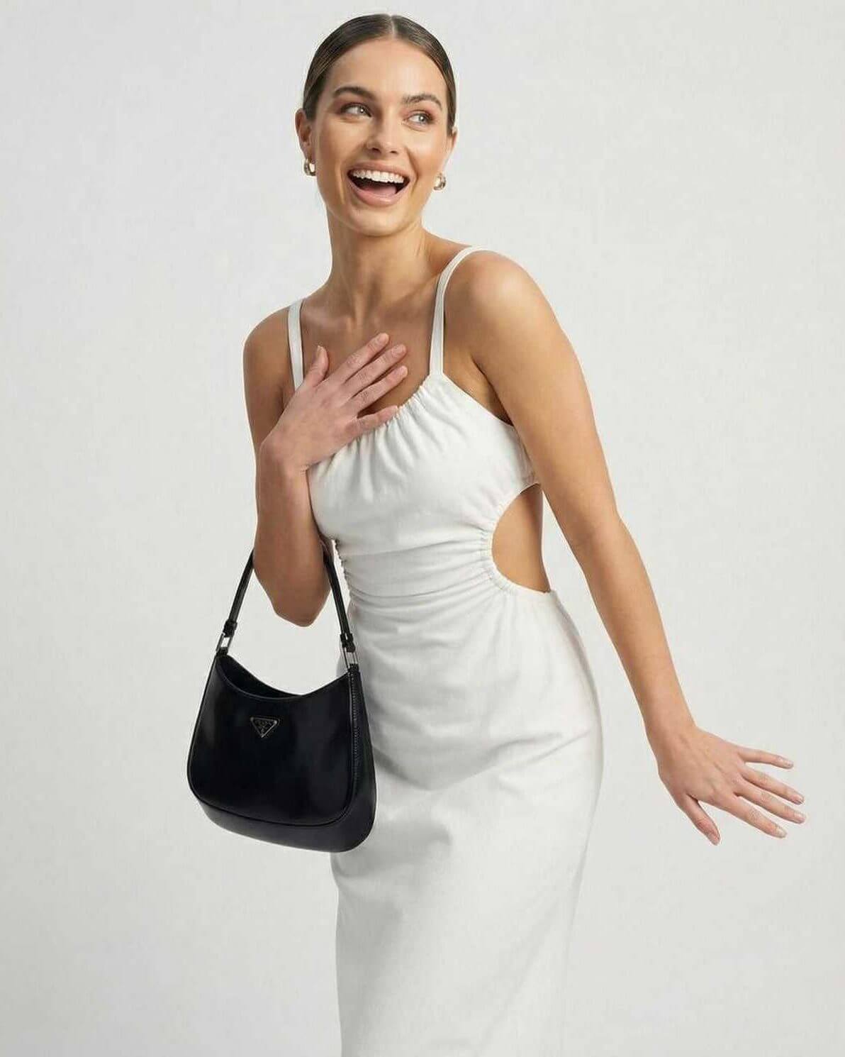 Woman smiling in a white Celeste Midi Dress with a black handbag, showcasing elegant fashion by Lauven.