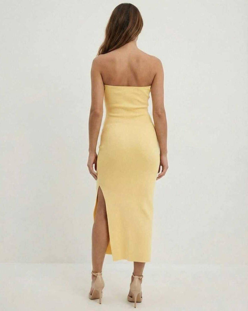 Back view of a woman wearing the Celeste Midi Dress by Lauven, a strapless yellow sheath dress with a side slit.