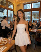 Lauven Luna Mini Dress displayed in a dining setting, featuring a strapless design and A-line silhouette in classic white.