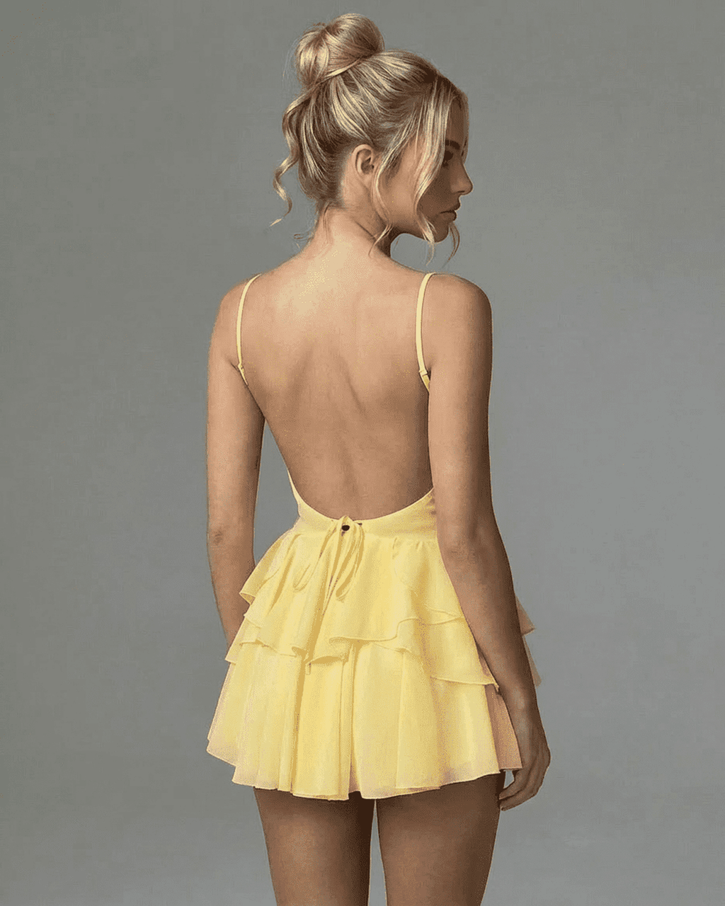 Back view of a model wearing the Marigold Mini Dress by Lauven, showcasing its ruffled tiered skirt and spaghetti straps.