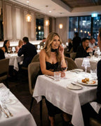 Noir Maxi Dress worn by a smiling woman at a fine dining restaurant, showcasing elegance and sophistication.