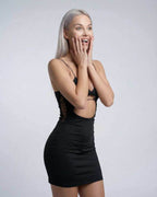 Excited model wearing Lauven Nova Mini Dress, featuring cutout detail and spaghetti straps in black.