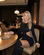 Chic woman in a Nova Mini Dress by Lauven, elegantly seated at a restaurant table with wine and food.