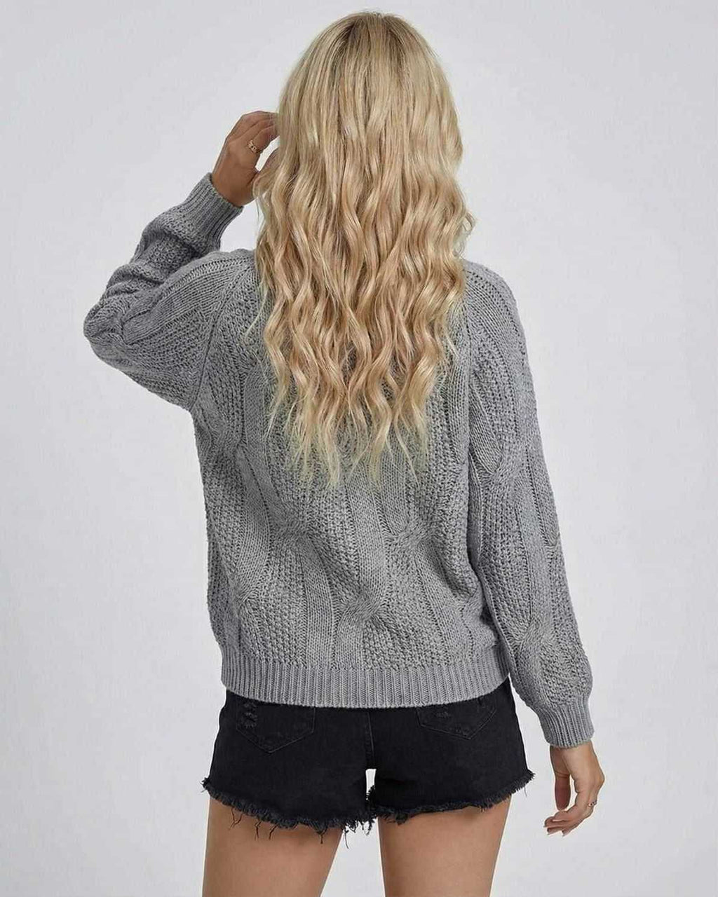 Back view of a woman wearing the grey Orion Sweater by Lauven, showcasing its cable-knit texture and long sleeves.