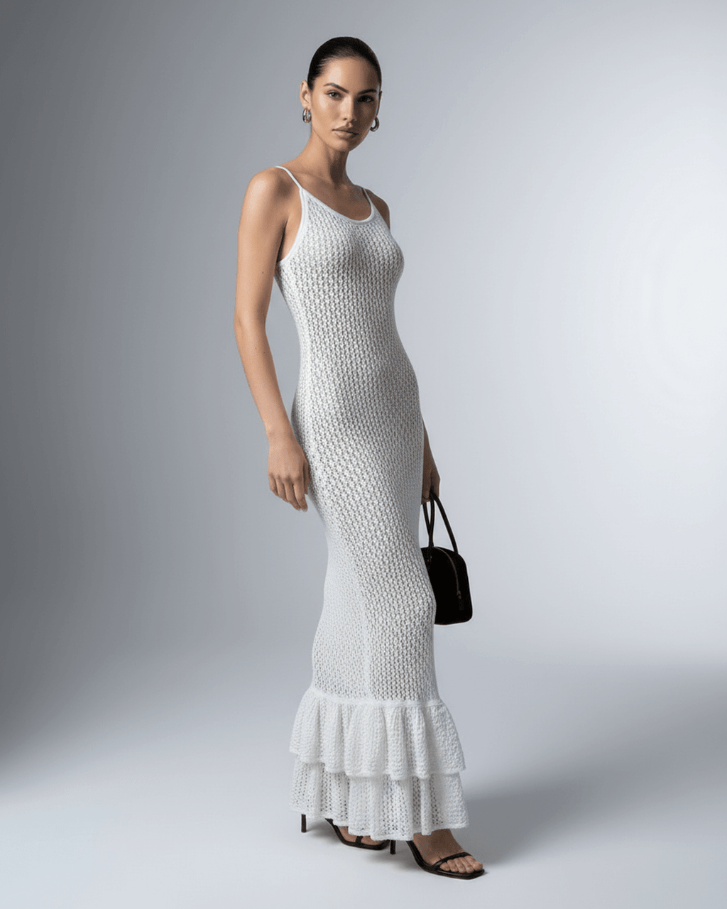 Model wearing Lauven Pearl Maxi Dress, a white hollow out bodycon dress with a ruffled hem.