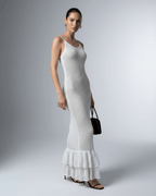 Model wearing Lauven Pearl Maxi Dress, a white hollow out bodycon dress with a ruffled hem.