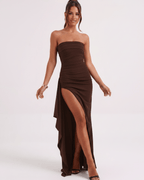 Model wearing the Solenne Maxi Dress, a strapless brown polyester dress with a dramatic side slit and an asymmetric panel.