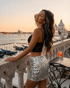 Stylish model wearing the Sterling Mini Skirt by Lauven, showcasing its silver sequin hem against a scenic waterfront backdrop.