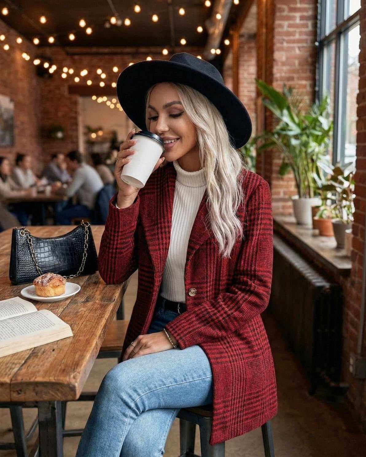 Woman wearing the Verona Jacket by Lauven, sipping coffee in a cozy café with a stylish black hat.