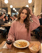 Woman wearing a dusty rose Verona Sweater by Lauven, enjoying dinner at a restaurant with wine and pasta.