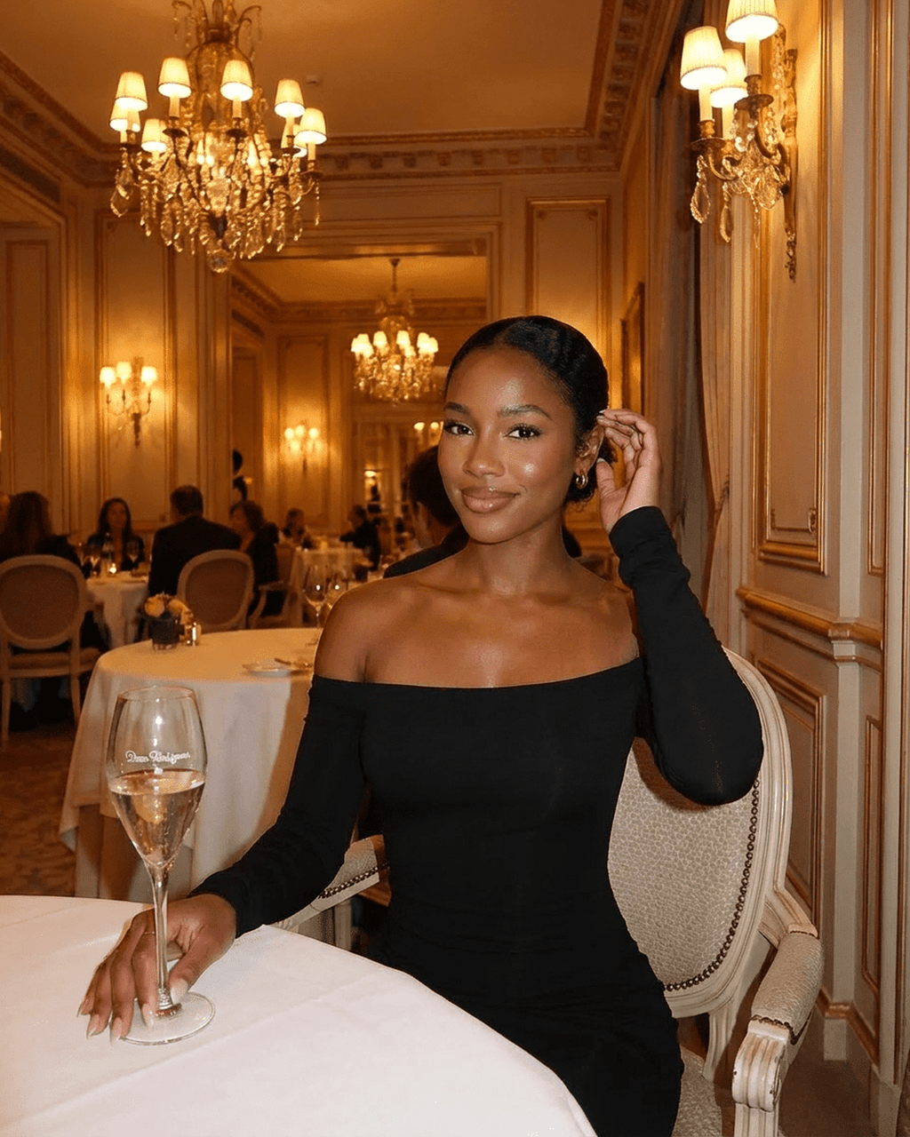 Elegant woman in Nocturne Maxi Dress by Lauven, off-shoulder style, seated in a luxurious dining setting.