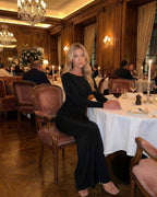 Elegant woman wearing Lauven Noir Maxi Dress, showcasing long sleeves and open back in a refined dining setting.
