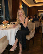 Model wearing Noir Maxi Dress by Lauven, an elegant black dress with square neckline, at a dining table in a luxurious restaurant.
