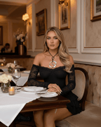 Elegant woman wearing Noir Mini Dress from Lauven, featuring black lace and ruffled hem, dining in a sophisticated restaurant.