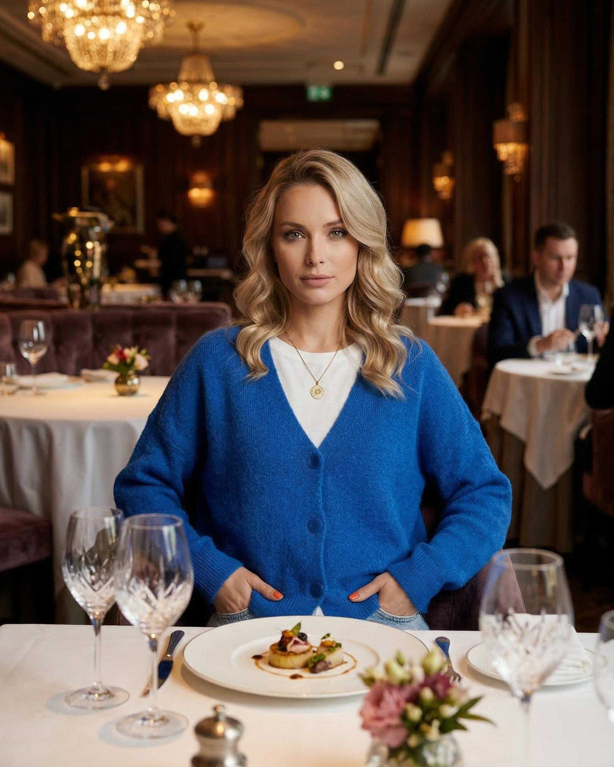Nova Cardigan by Lauven worn by a woman in a restaurant setting, showcasing vibrant blue knitwear and elegant dining.