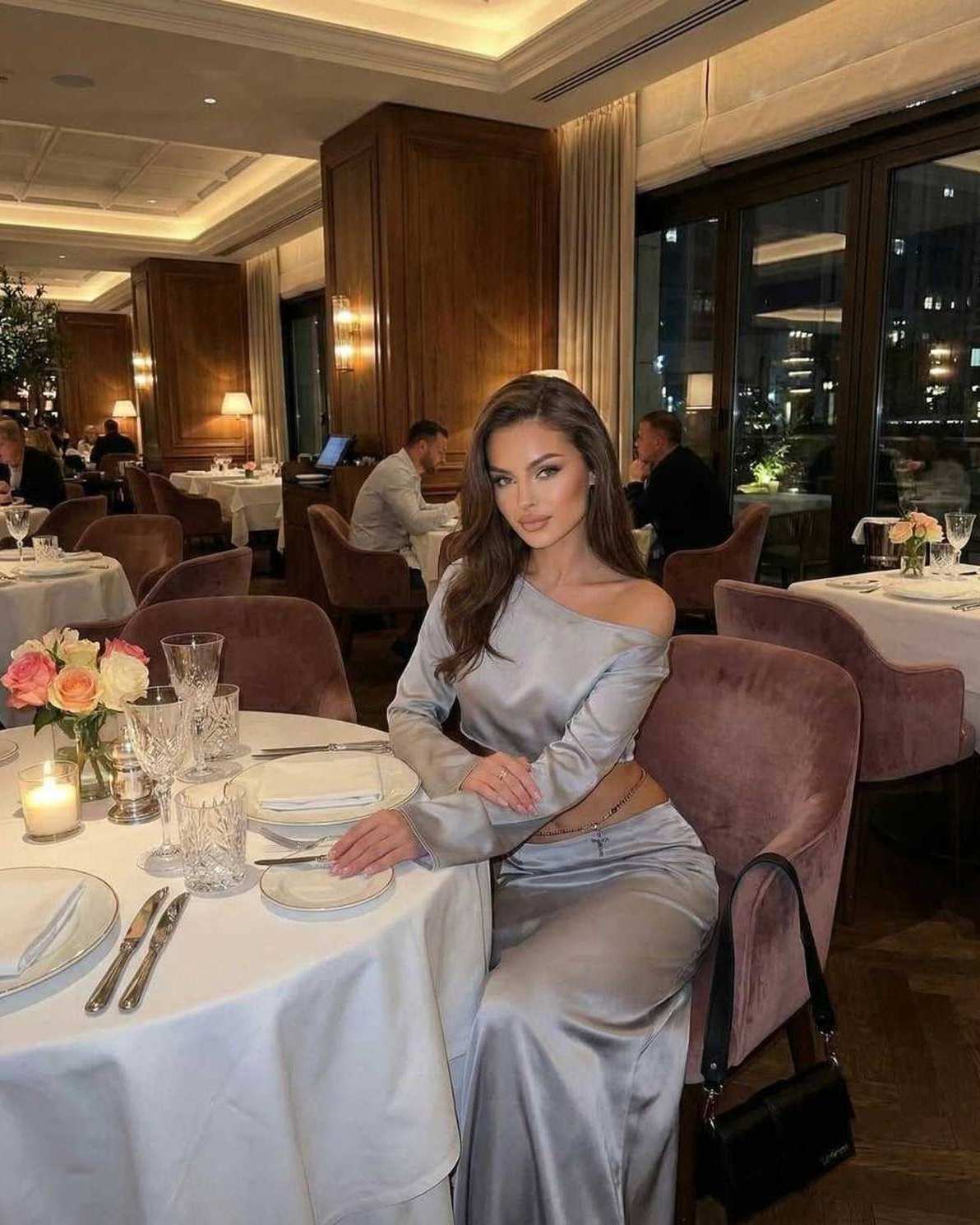 Nova Midi Dress by Lauven worn by a woman in a chic restaurant setting, showcasing its elegant silver fabric and silhouette.