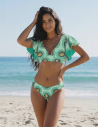 Lauven Kiwi Two-Piece Swimsuit featuring green kiwi print, deep V-neckline, and flutter sleeves at the beach.