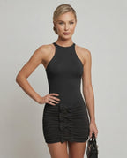 Model wearing the Lyra Mini Dress by Lauven, a sleek black bodycon dress with ruched skirt and bow accents.