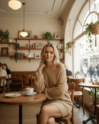 Sahara Mini Dress by Lauven, warm beige oversized knitted dress in cozy café setting.