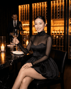 Elegant woman in Selene Mini Dress by Lauven, seated at a restaurant, holding a wine glass, exuding sophistication.
