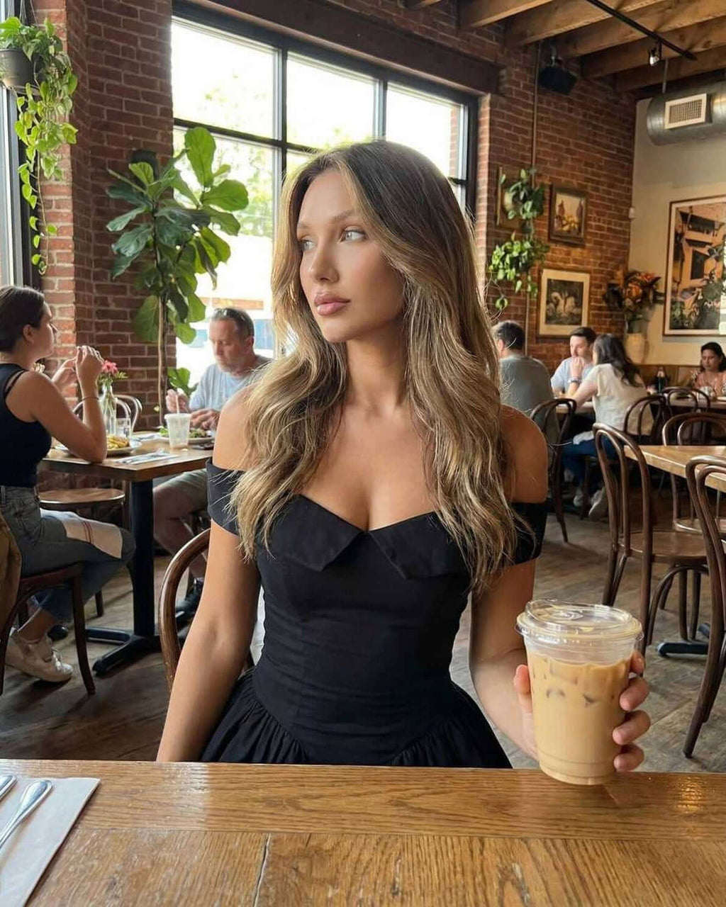 Selene Mini Dress by Lauven, showcasing a model wearing the sleek black dress with a drink at a trendy café.