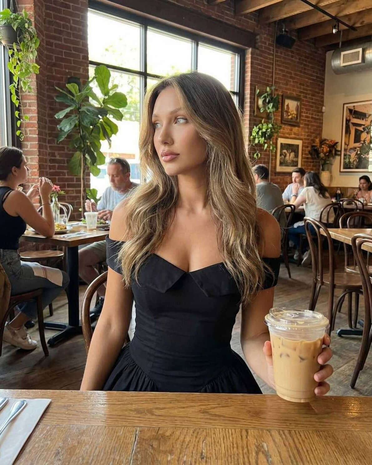 Selene Mini Dress by Lauven, showcasing a model wearing the sleek black dress with a drink at a trendy café.