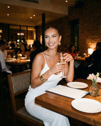 Elegant woman enjoying dinner in a Seraphina Maxi Dress by Lauven, showcasing a stylish white spaghetti strap design.