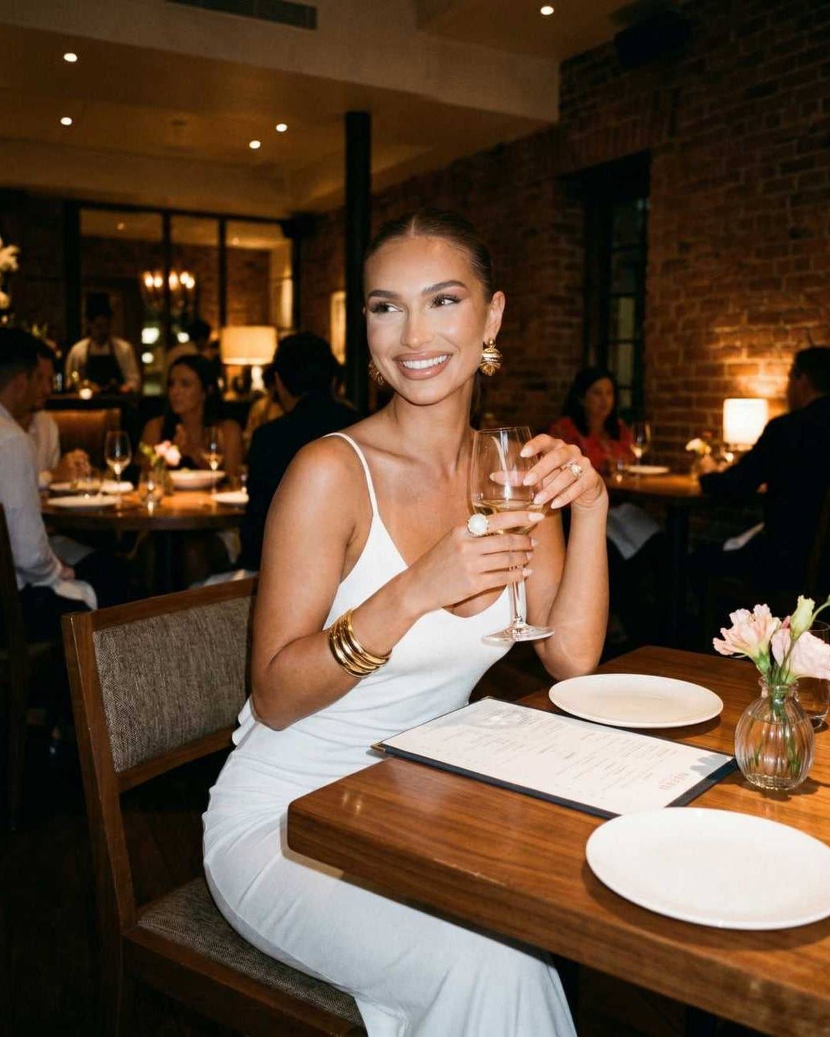 Elegant woman enjoying dinner in a Seraphina Maxi Dress by Lauven, showcasing a stylish white spaghetti strap design.